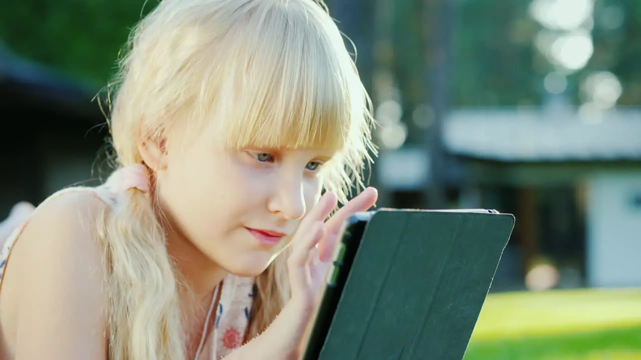 Portrait Of A 6 Year Old Girl Playing On A Tablet Lies On The Grass Near The House 4k 10 Bit Video