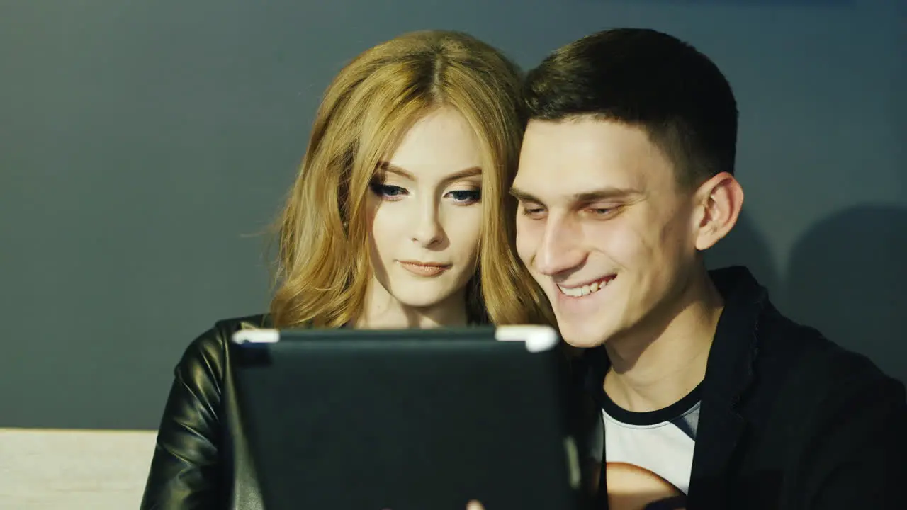 Young Couple 20-25 Years Uses The Tablet In A Cafe They Laugh And Smile