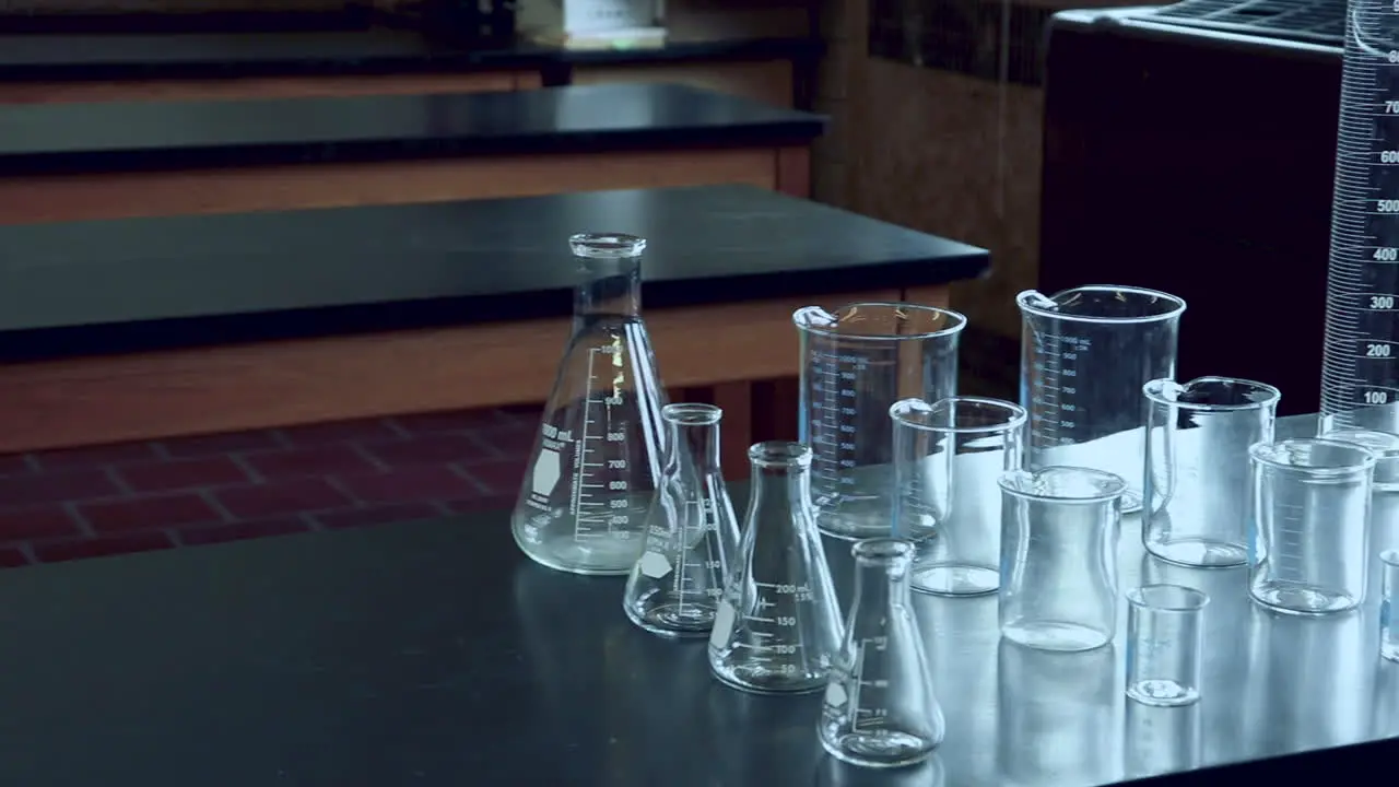 Panning across black lab bench with a variety of chemical glassware in high school chemistry lab