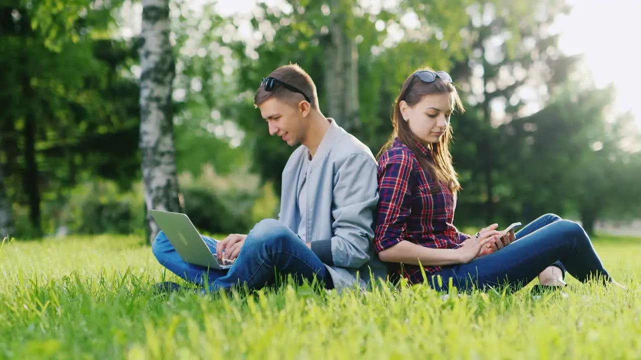 Couple Resting In A Park A Man Uses A Laptop Woman Typing On Smartphone Hd Video