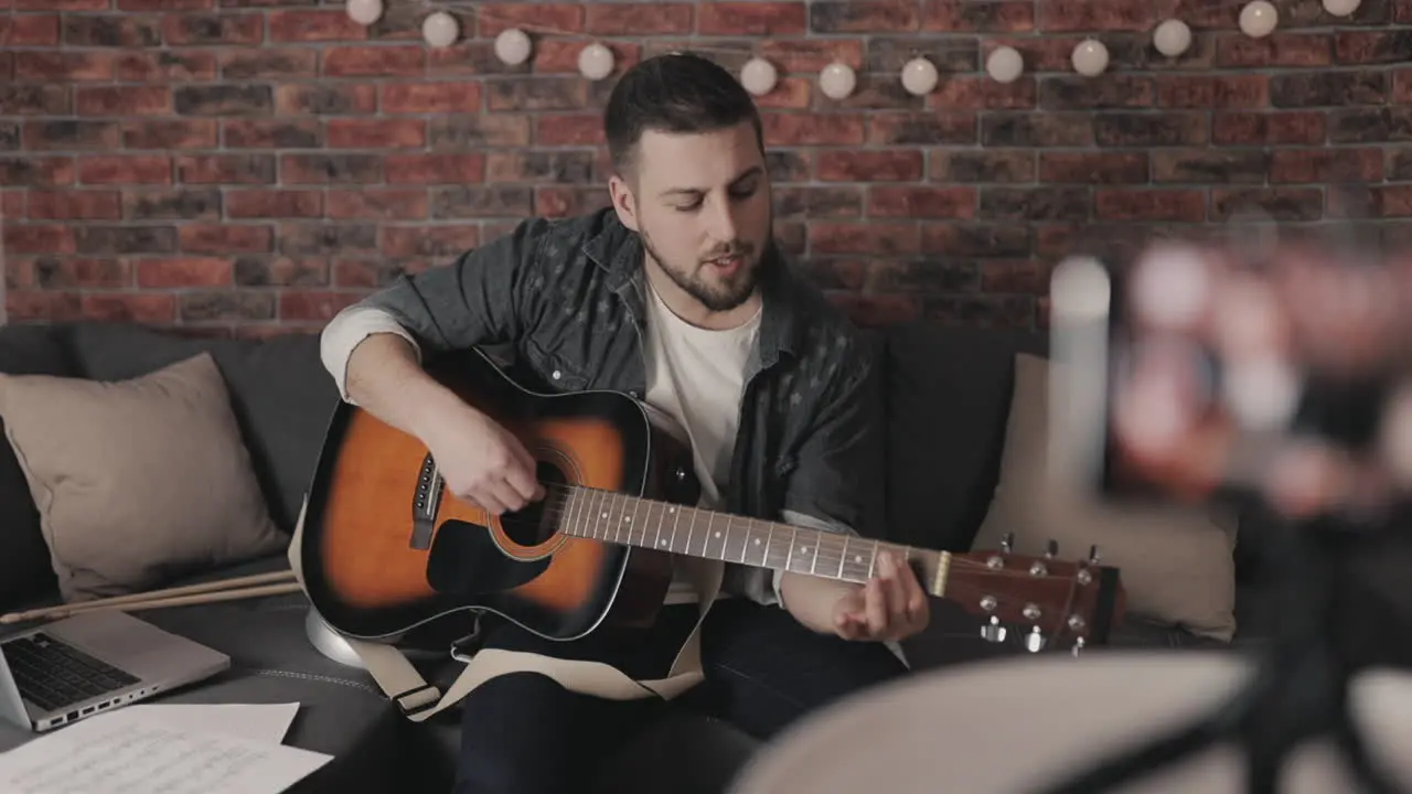 Young Male Musician Streaming A Video Tutorial About Playing Guitar At Home