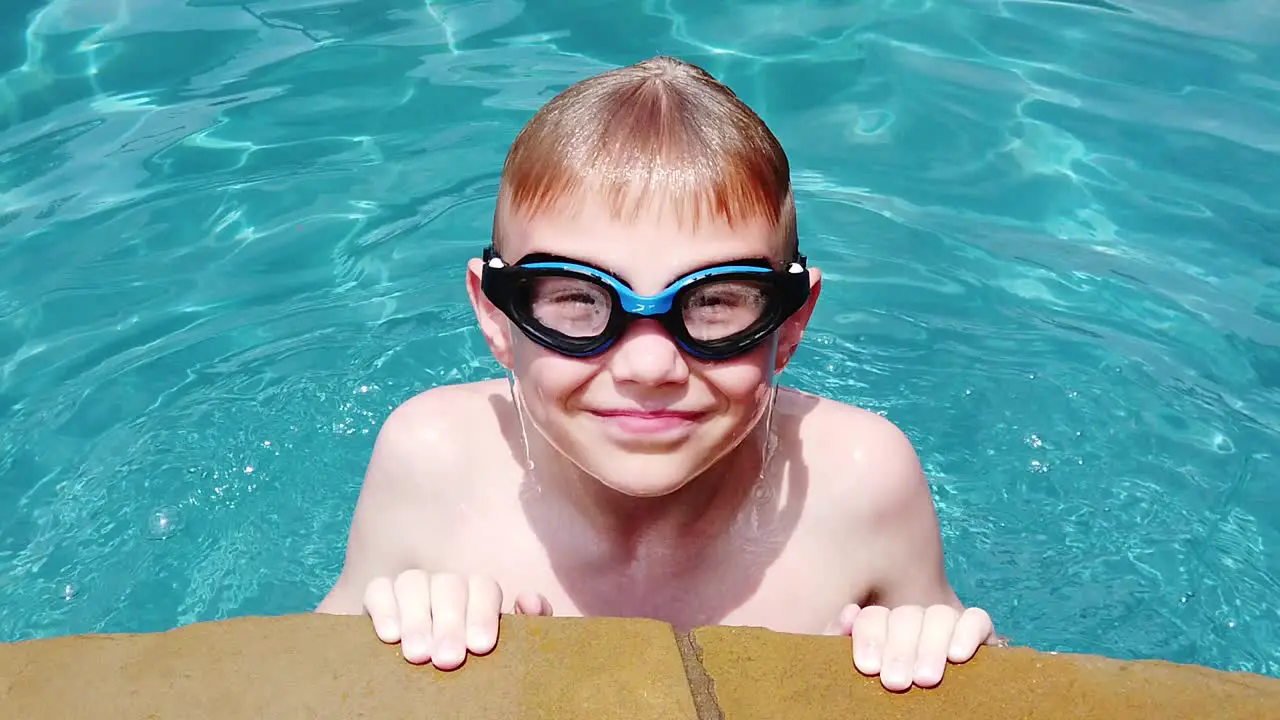 Young Caucasian boy age 10 coming out of the water in a pool in slow motion with goggles and smiling