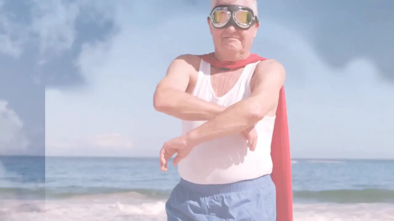 Animation of clouds over senior caucasian man wearing superhero costume on beach