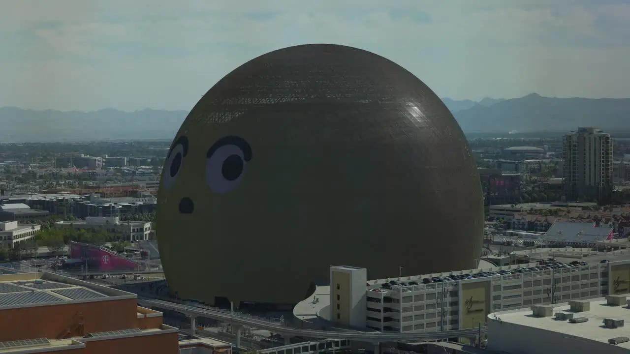 Illuminated MSG Sphere With Yellow Emoji Face On Surface Looking Around During The Day