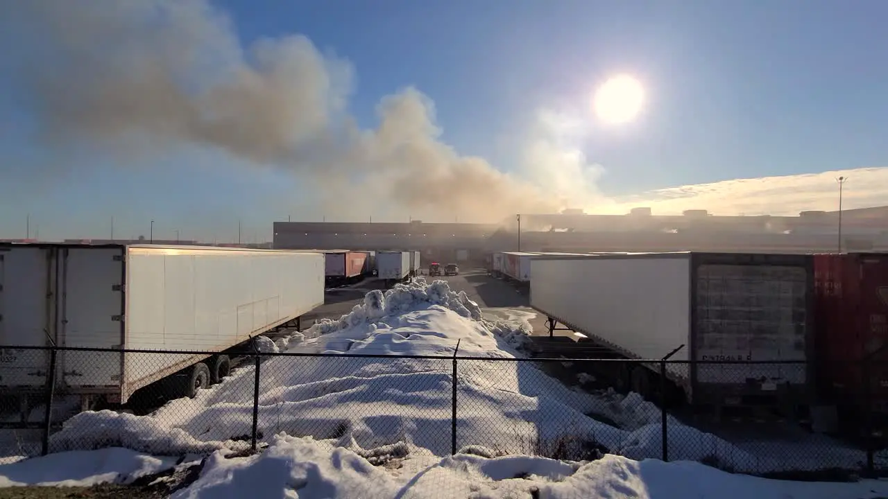 Large shipping containers are parked in factory depot by snow piles at midday