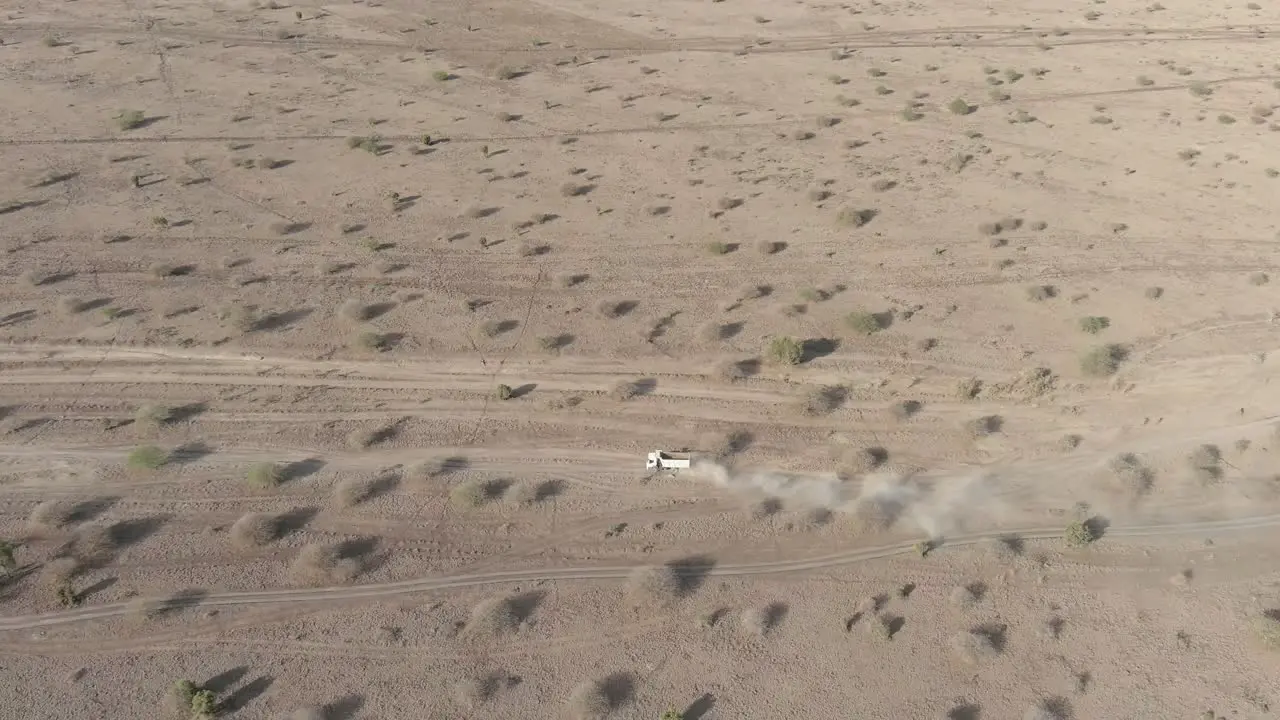 An aerial view of a white truck driving along a dirt road