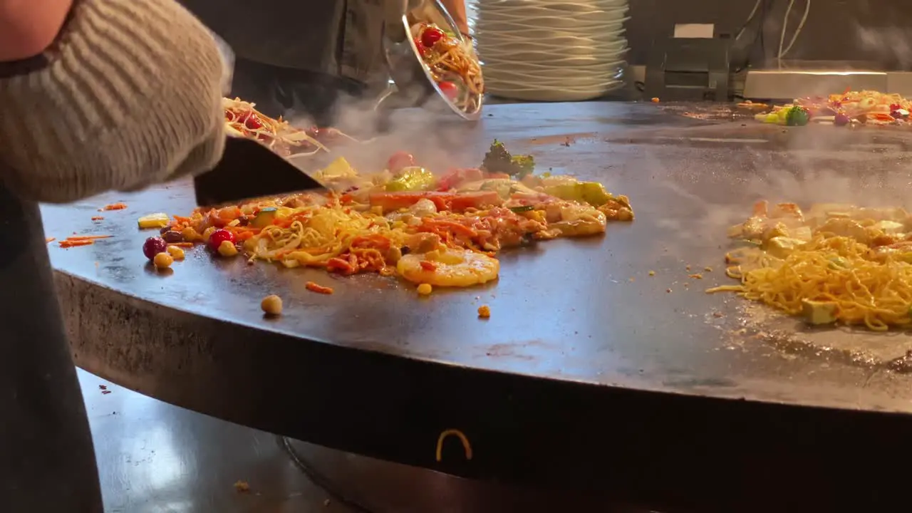 Chef Playing Skillful Tricks while Stir Frying on a Large Stove at a Mongolian Grill