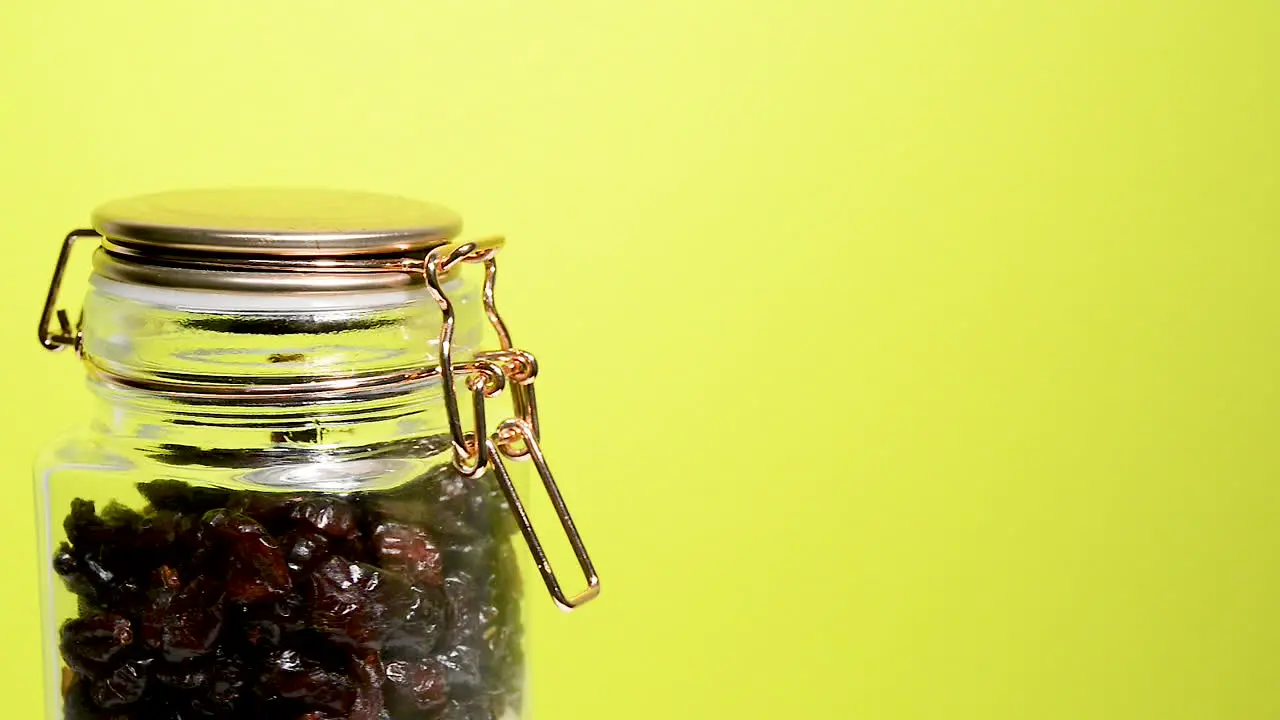 Detail of an airtight mason jar rotating with dehydrated cranberry on a neon yellow background