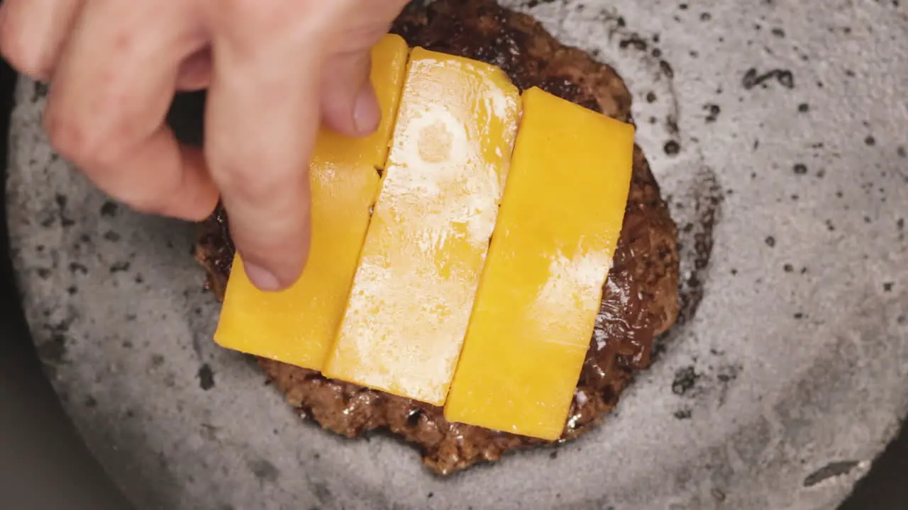 Top Close up View on Man Hand Adding Three Slices of Cheddar Cheese on Hot Grilled Meat Patty