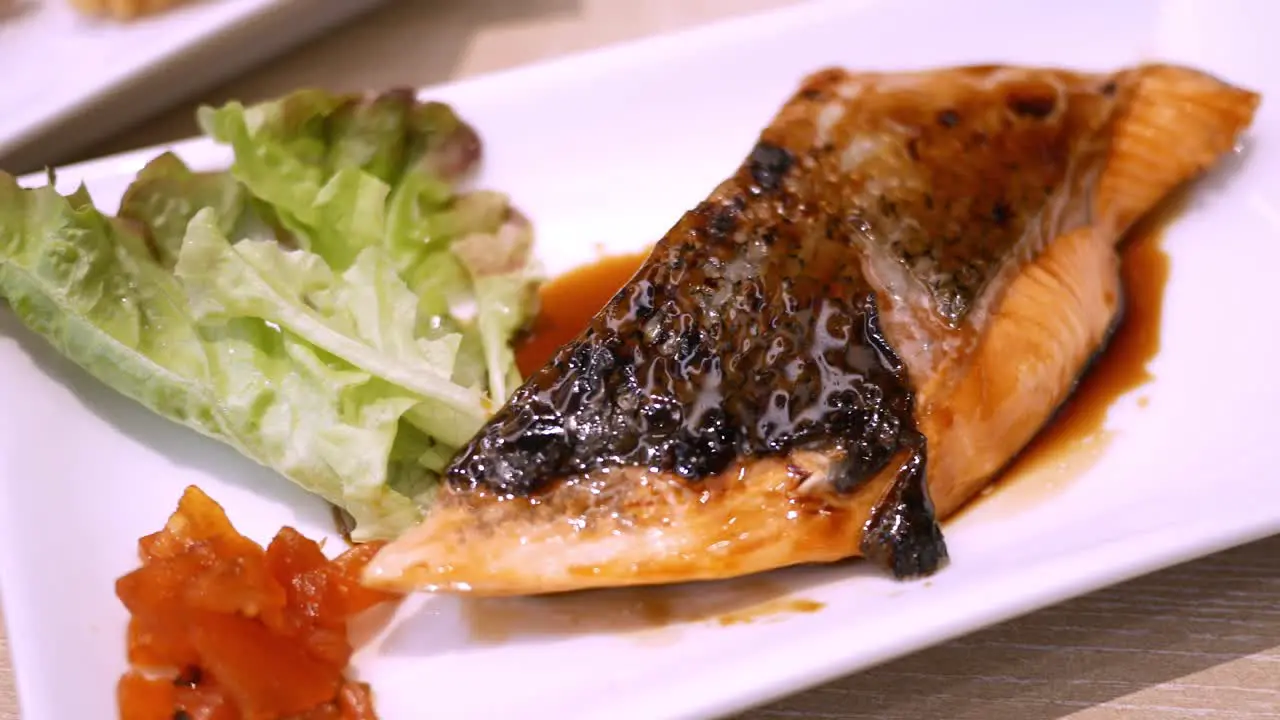 Panning from the right to the left side of the frame showing a platter of grilled salmon steak glazed with teriyaki sauce