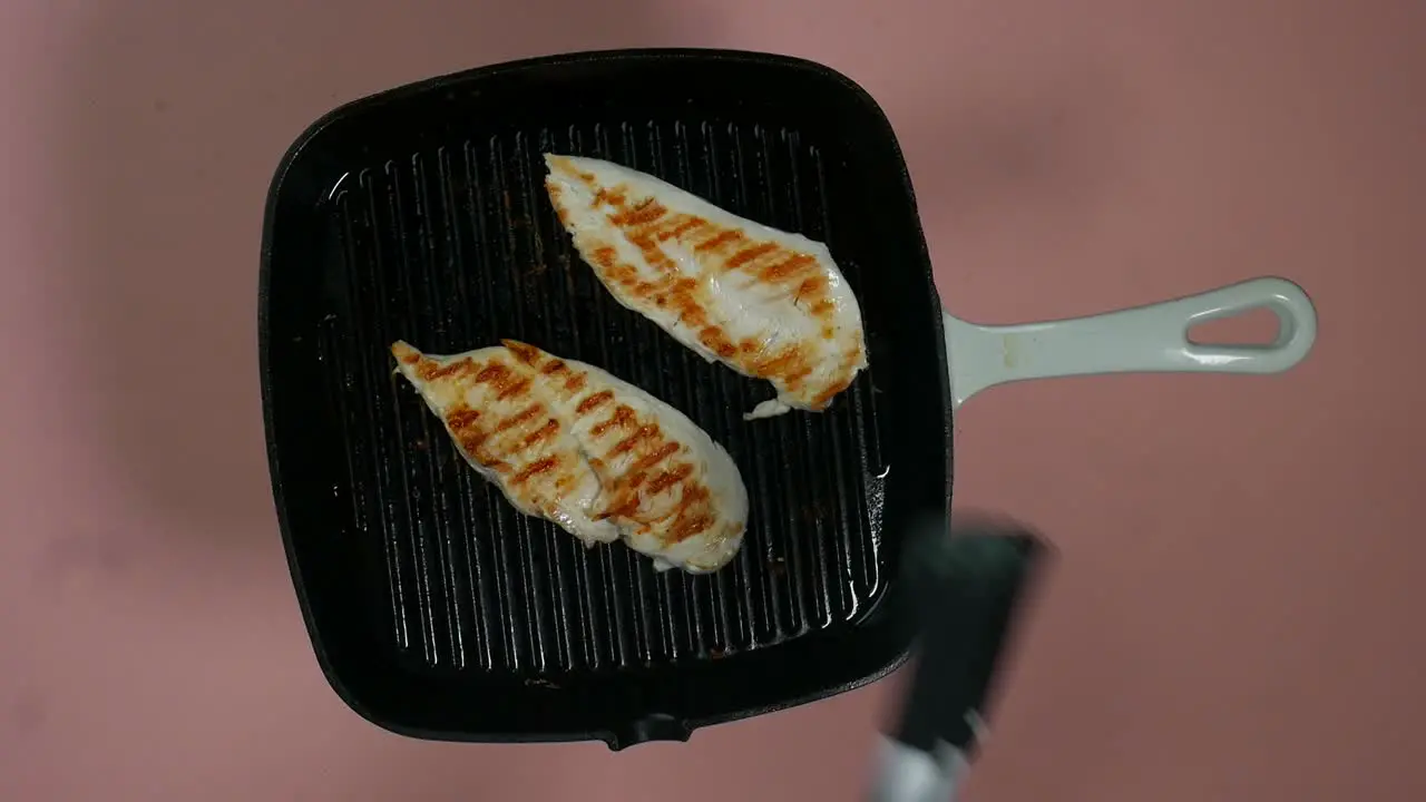 Top view of turning over cooked and greased chicken breast fillet