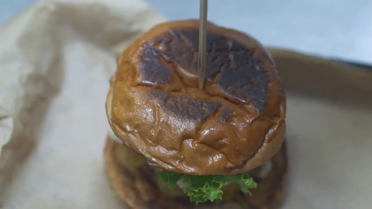 A large toothpick is placed in the top of a gourmet burger at a restaurant as the final touch