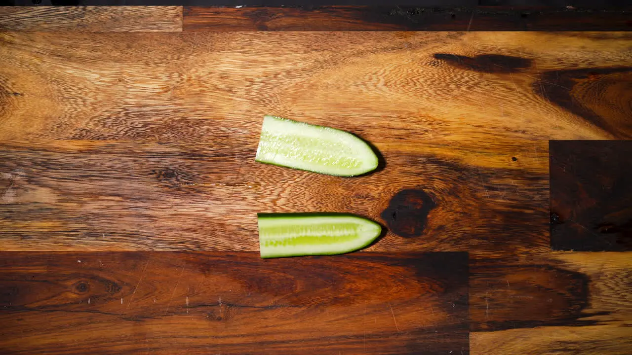 Top view of a male hand slicing half a cucumber in half perpendicular