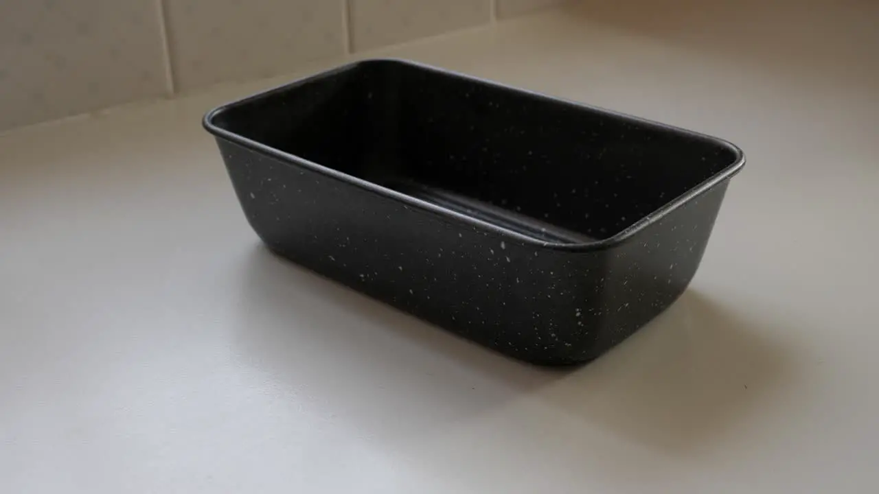 Person places metal tray on table and tries to line with baking paper on kitchen bench