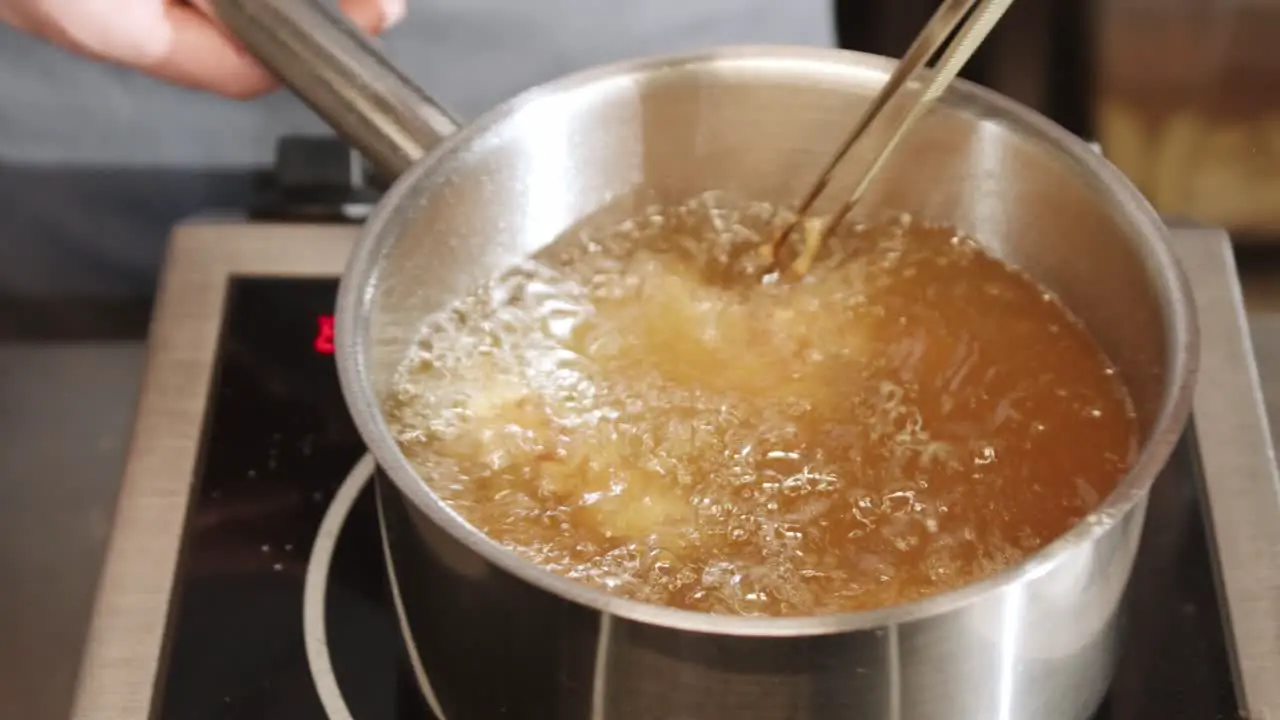 Person is frying chicken at home using heated oil in pan for deep frying slowly rotating and spinning it into pan