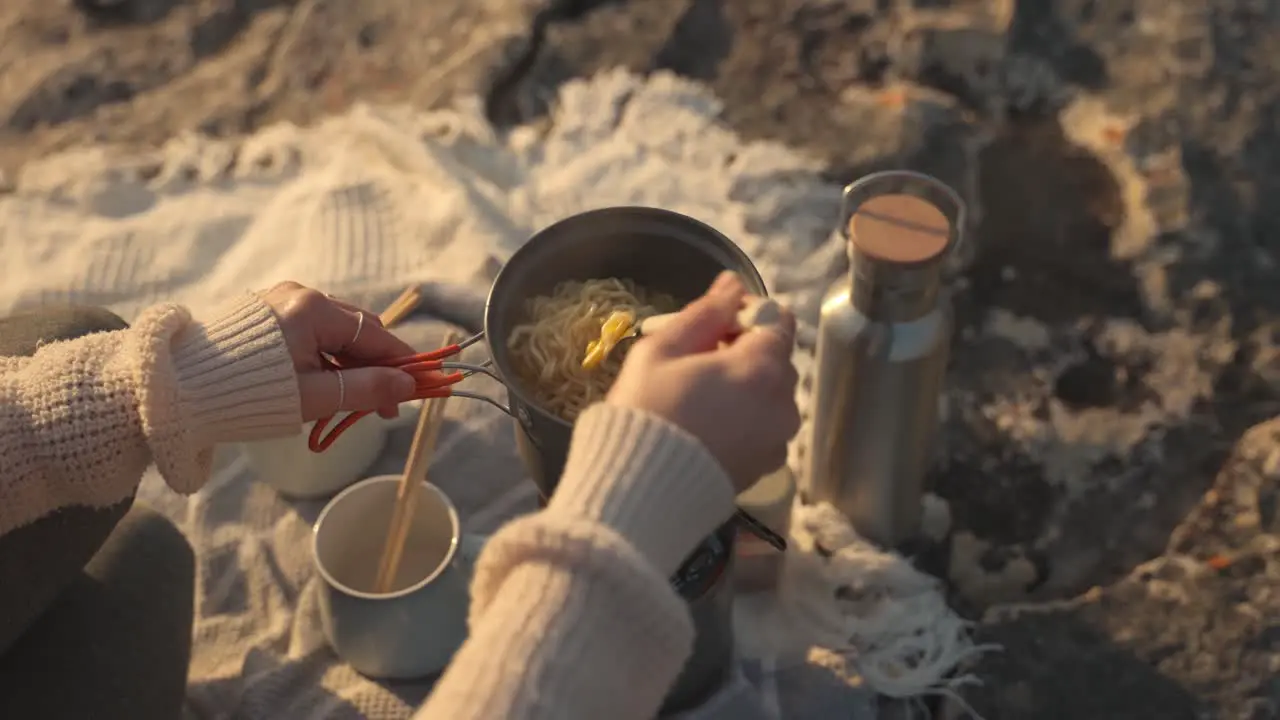 Slow motion footage of a woman cooking noodles in a small pot outdoors at sunset