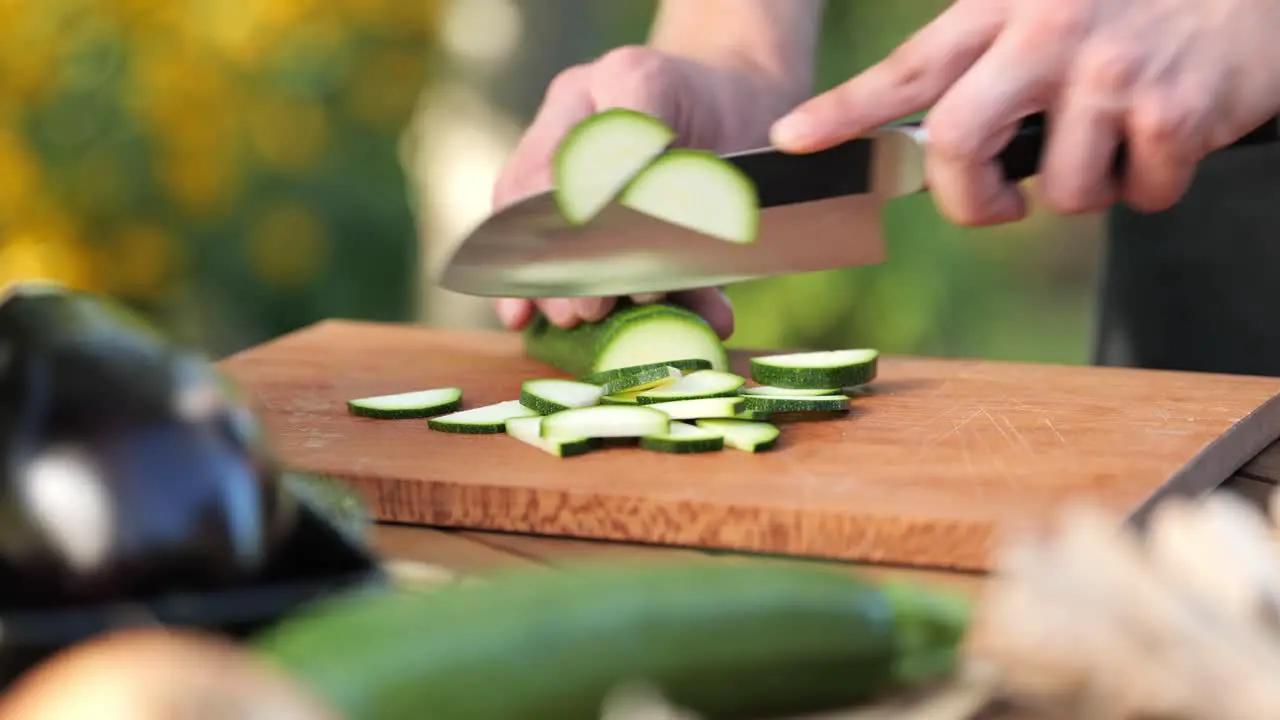 Young man cutting zucchini on a wooden board in his garden close up