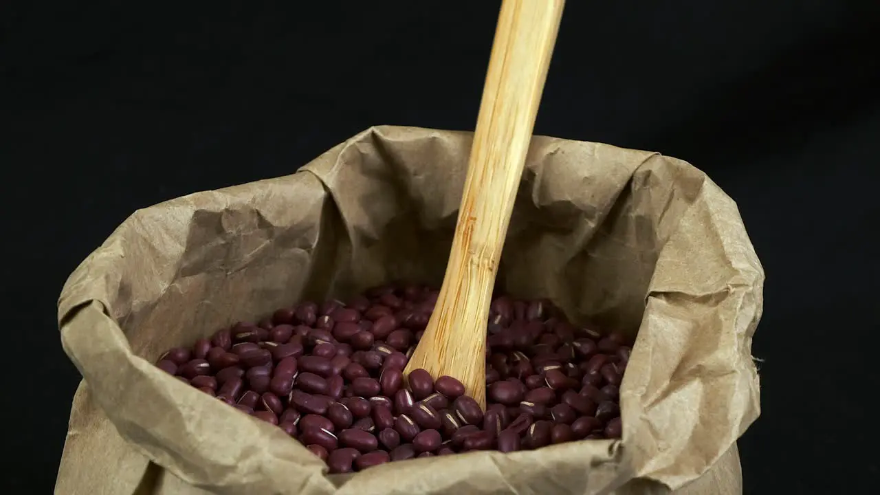 Nutritious dry red Adzuki beans rotate in paper bag with wooden spoon