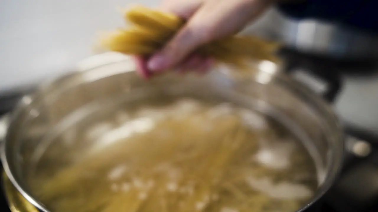 Cook breaking spaghetti noodles and dropping them into a pot in slow motion