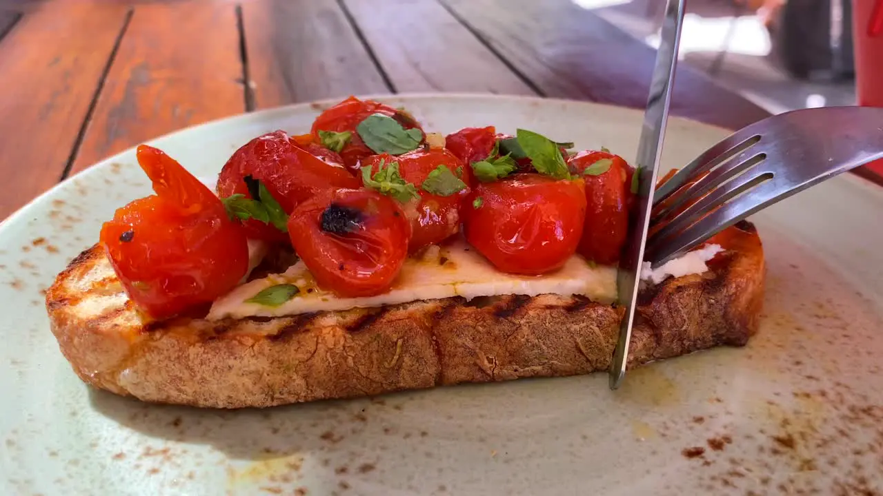 Cutting a delicious bruschetta sourdough toast with cherry tomatoes and fresh basil traditional italian breakfast brunch dish at a restaurant 4K shot