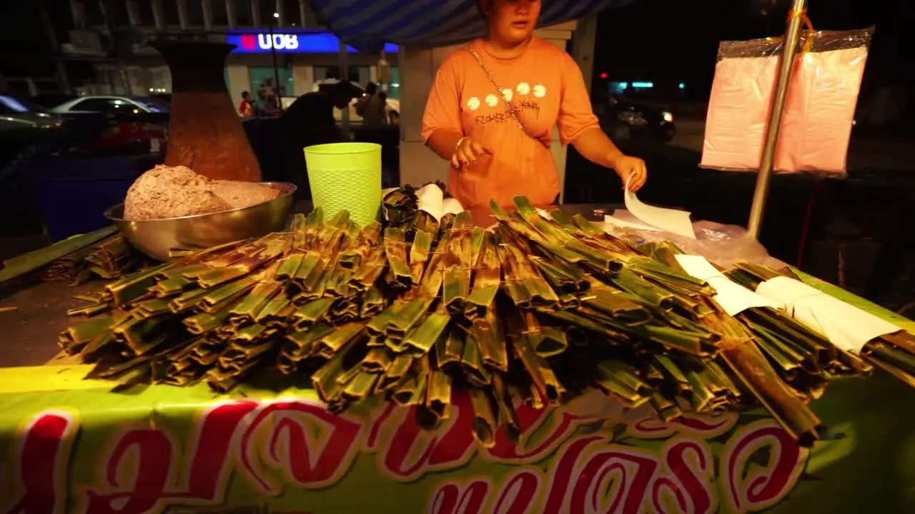 Woman cooking traditional Thai food in banana leafs at a night market