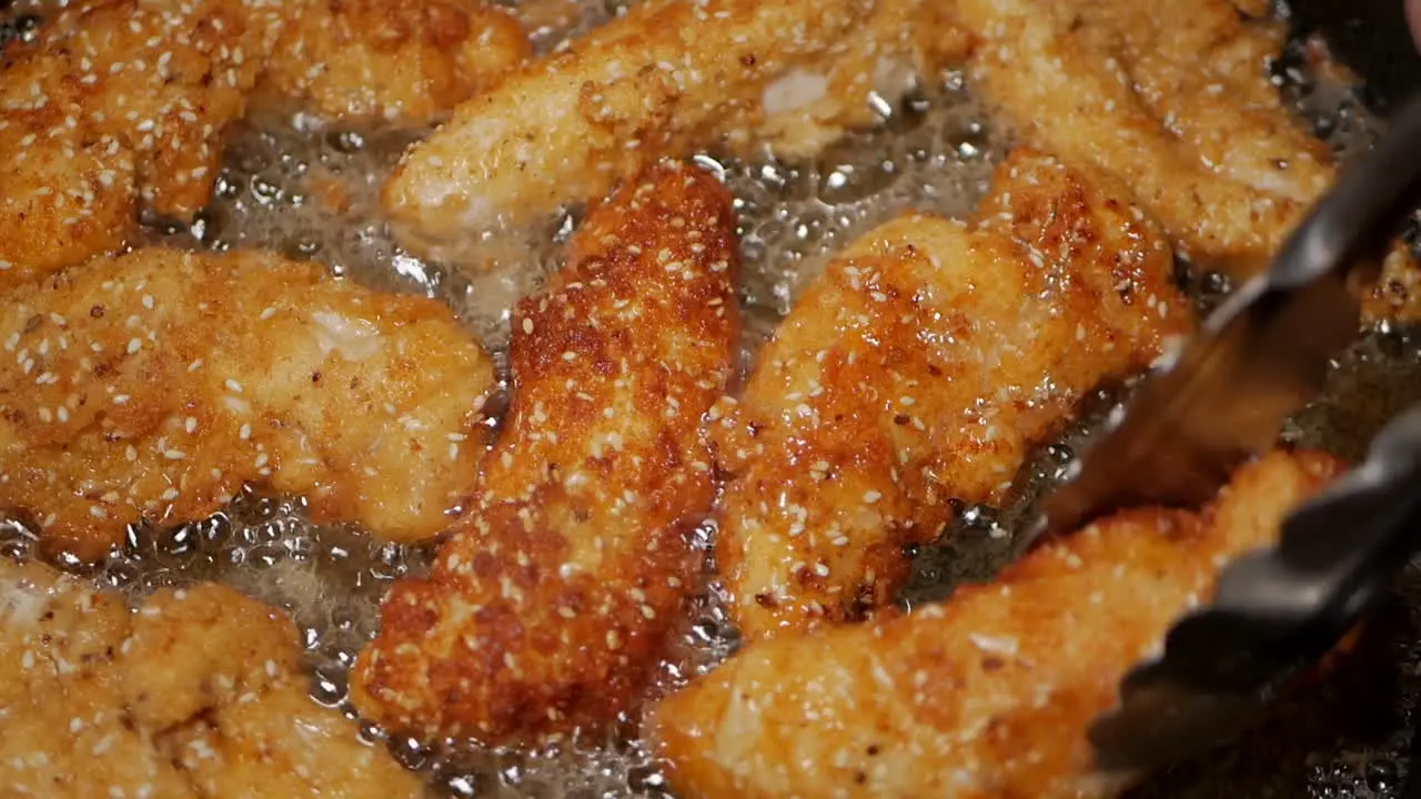 Crumbed breast chicken tenderloins turned in peanut oil in a pan with tongs