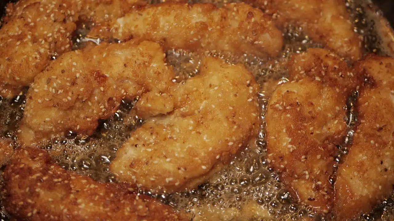 Crumbed breast chicken tenderloins fried in peanut oil in a pan