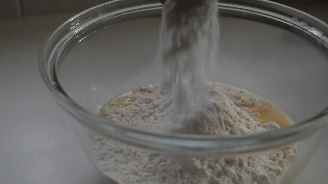 Male hand sprinkling baking powder from metal spoon into mix of flour and egg in glass bowl