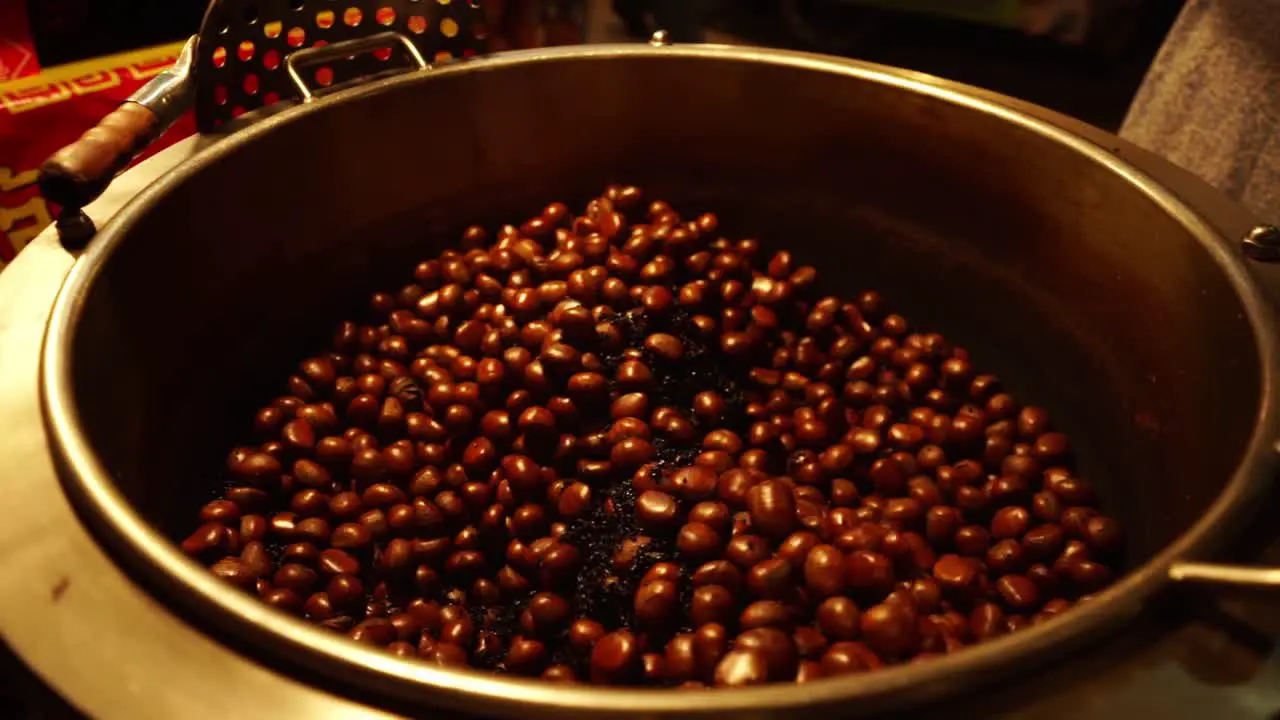 Slow motion footage of a street vendor's huge vat of fresh roasted chestnuts at a nighttime Thai market