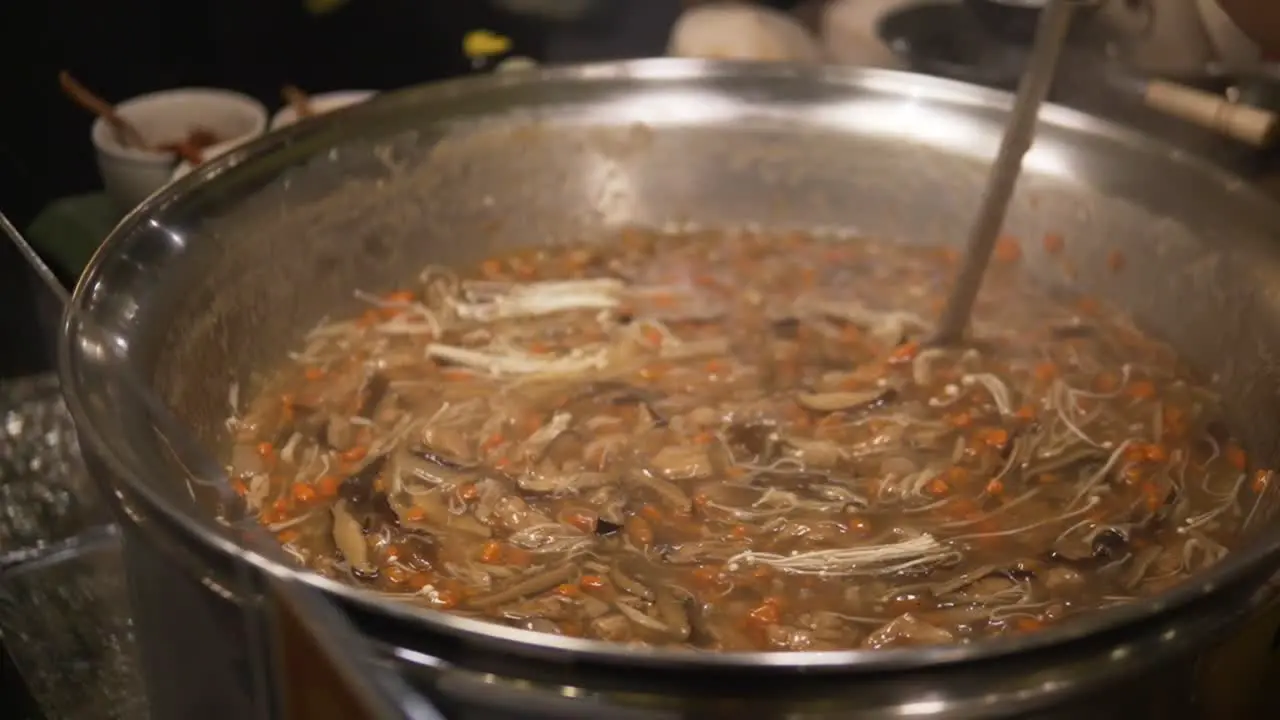 A woman in Bangkok is cooking food in a traditional Thai pot while stirring it