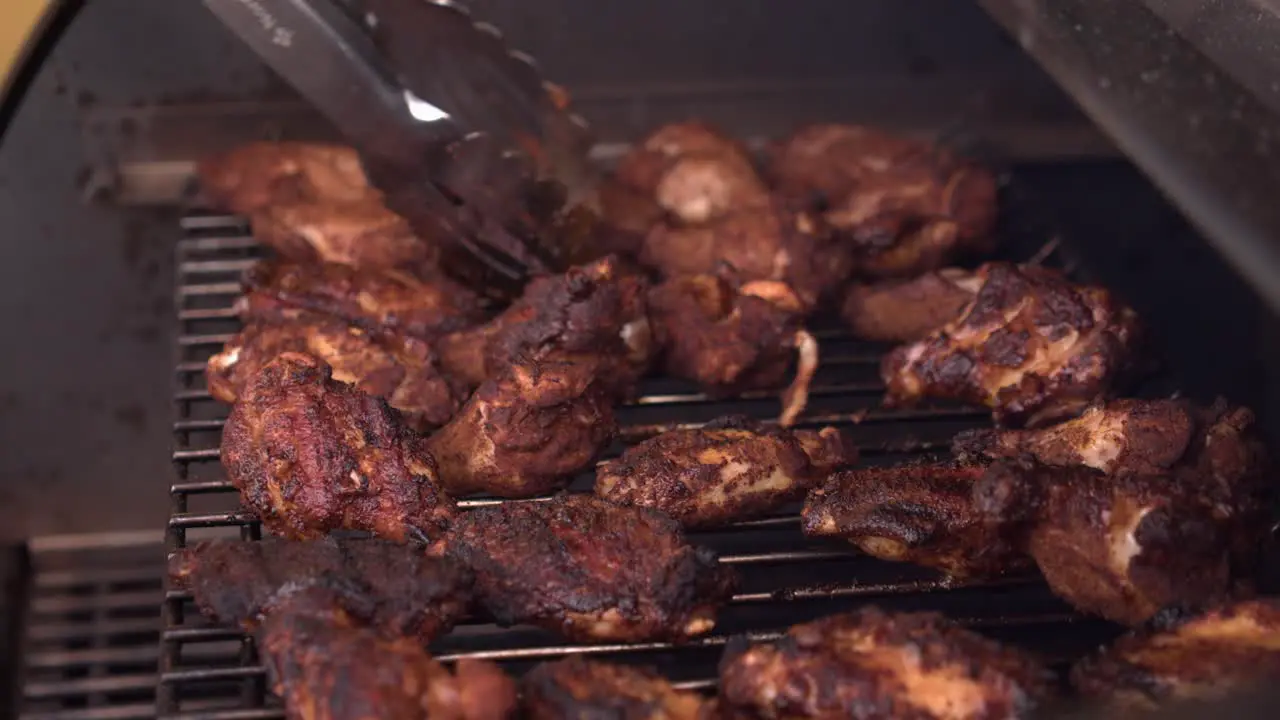 Chicken wings and drumsticks on hot BBQ grill are turned with tongs