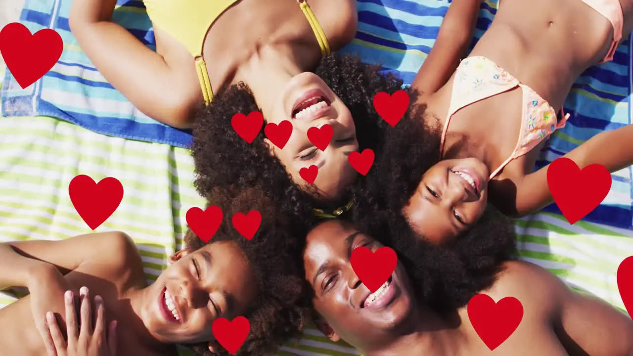 Animation of red hearts over smiling african american family on holiday lying on beach towels