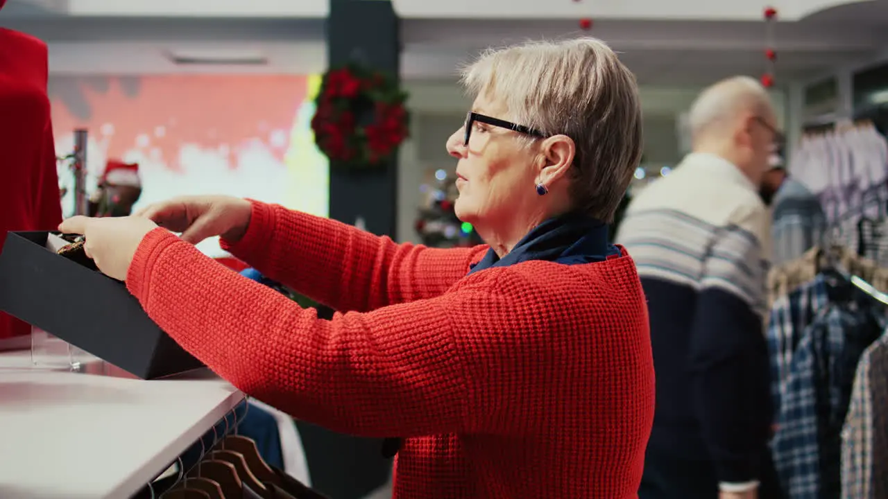 Elderly woman shopping for stylish neckties to gift husband for Christmas during winter holiday season Senior customer in xmas decorated clothing store looking for presents