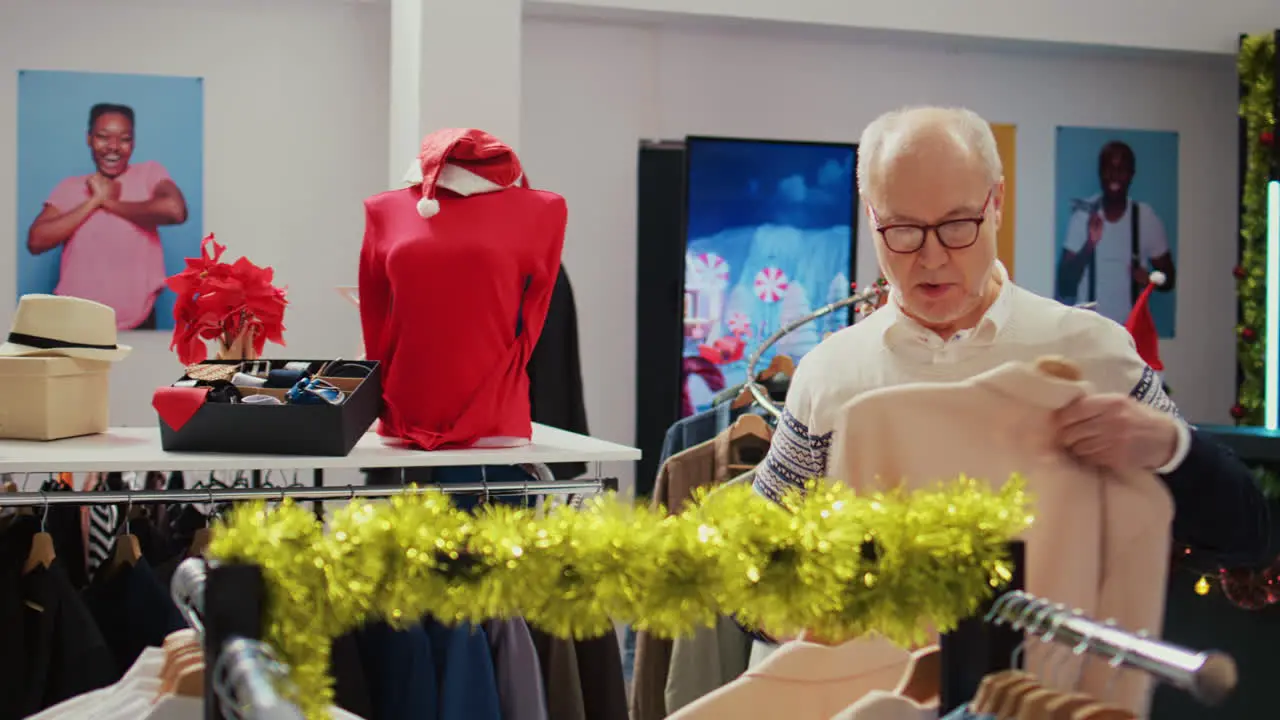 Octogenarian man in xmas decorated shopping mall store trying to determine if elegant blazer is the right fit Old shopper in Christmas adorn fashion boutique during winter holiday season