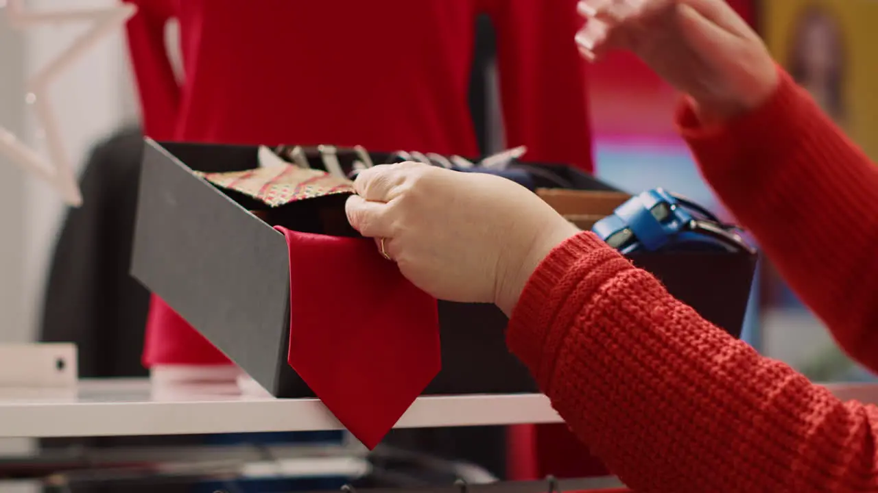 Close up shot of senior customer browsing through clothes in Christmas ornate clothing store trying to pick perfect necktie for son as xmas present during winter holiday season