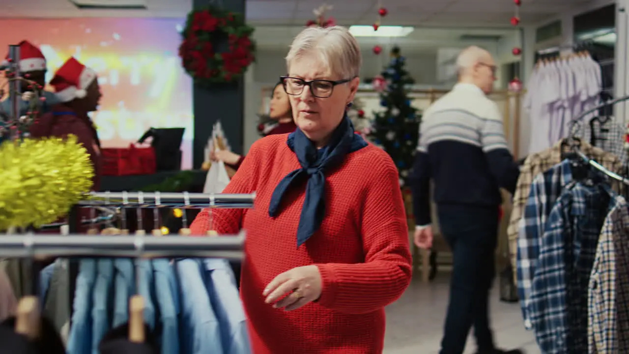 Elderly client browsing through clothes in festive xmas ornate shopping mall fashion shop men section looking for elegant shirt to gift husband for upcoming winter holiday season