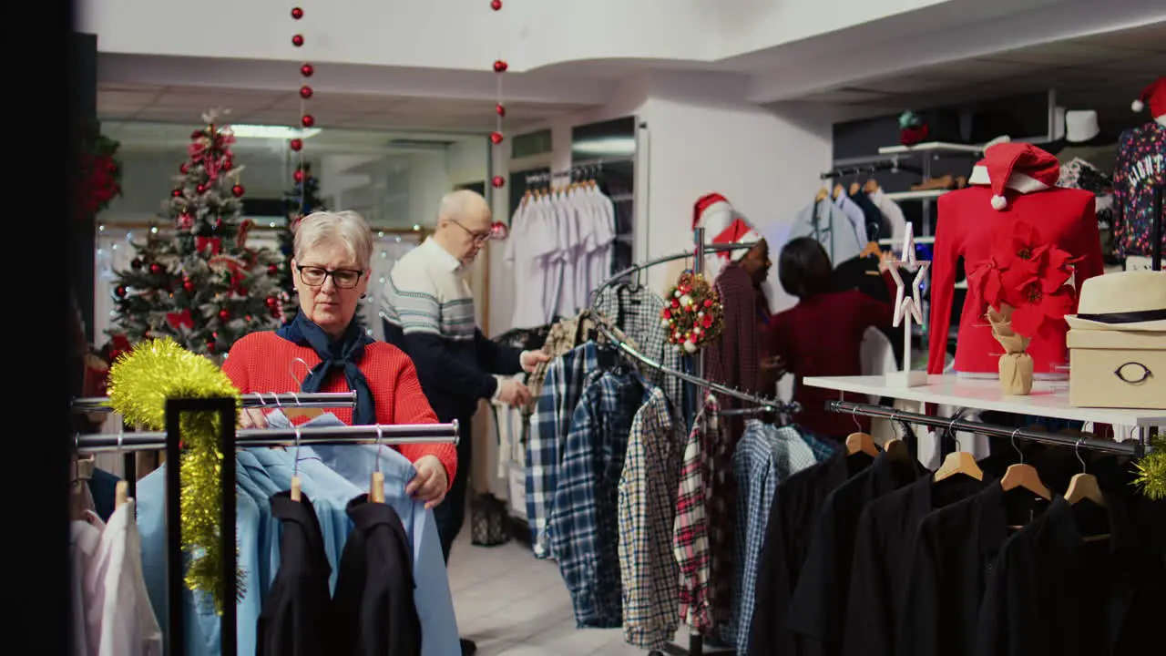 Customers roaming around busy clothing store decorated with Christmas ornaments during winter holiday season Clients shopping for gifts during xmas promotional sales in fashion boutique