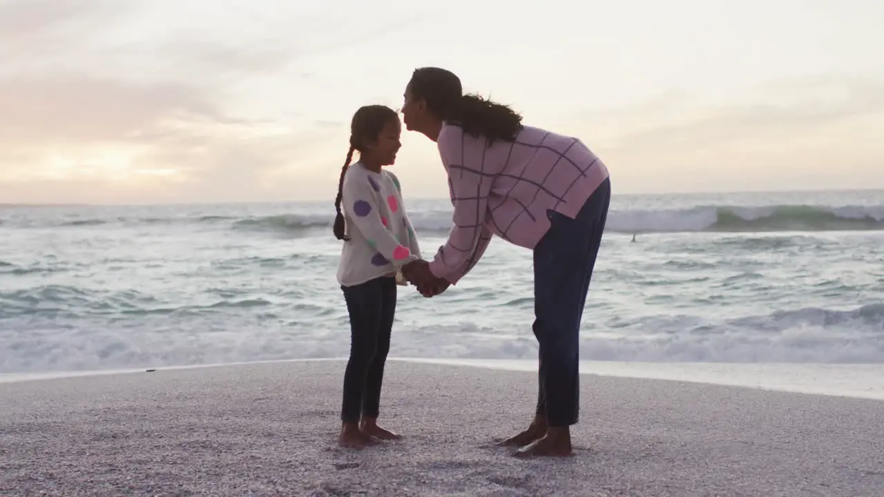 Happy hispanic mother kissing daughter on beach at sunset