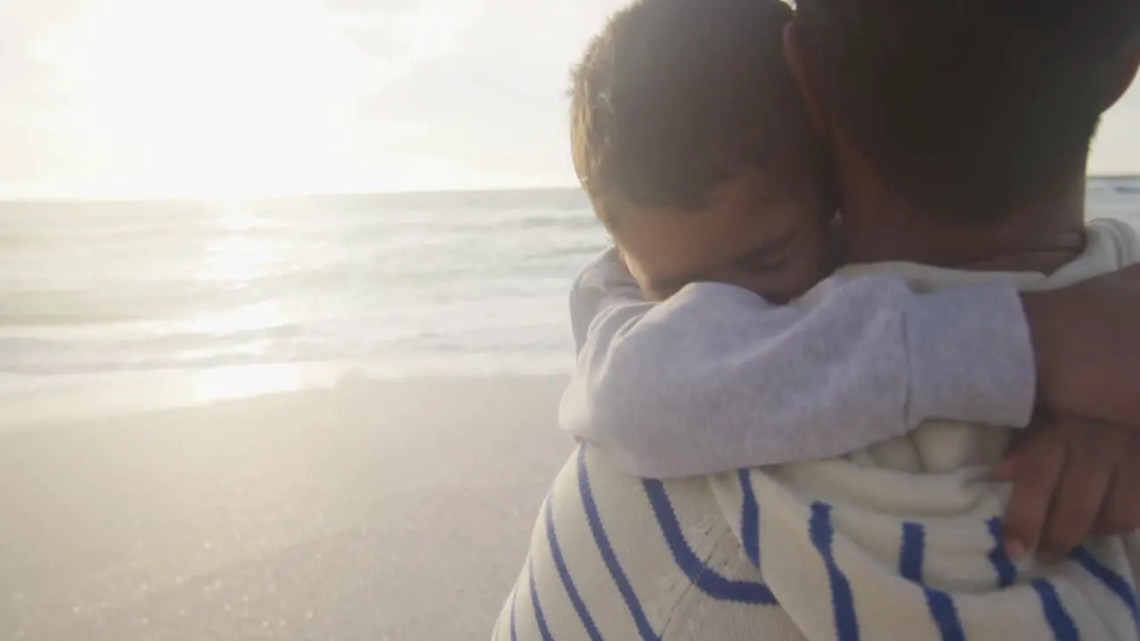 Portrait of hispanic father embracing son on beach at sunset