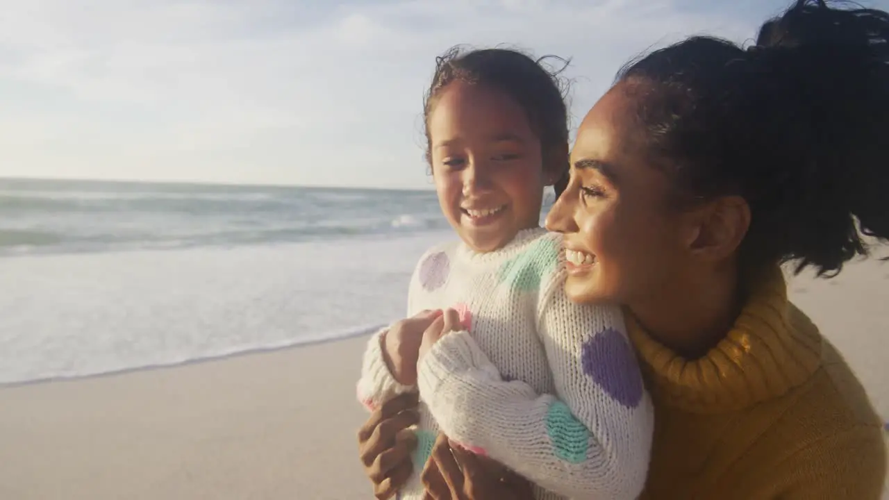 Portrait of happy hispanic mother and daughter embracing on beach at sunset