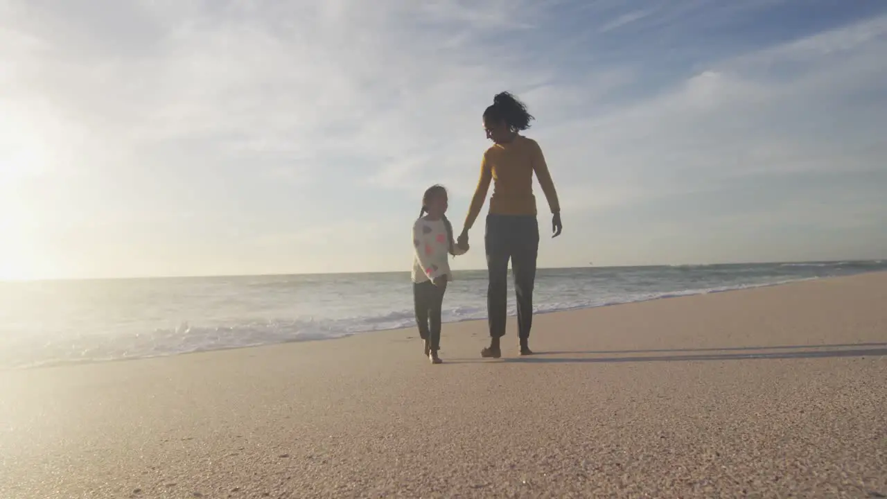 Happy hispanic mother and daughter walking on beach at sunset