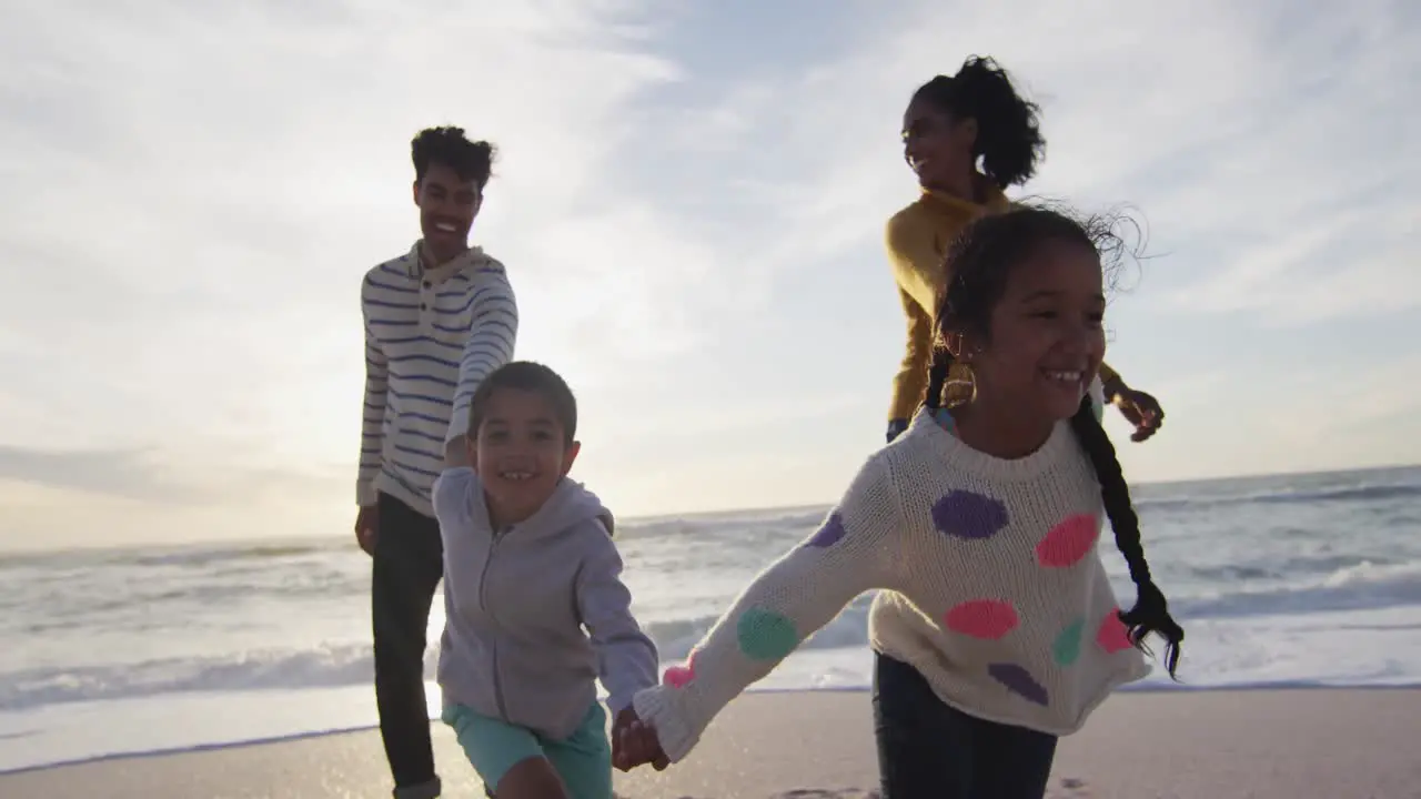 Happy hispanic familyholding hands and walking on beach at sunset