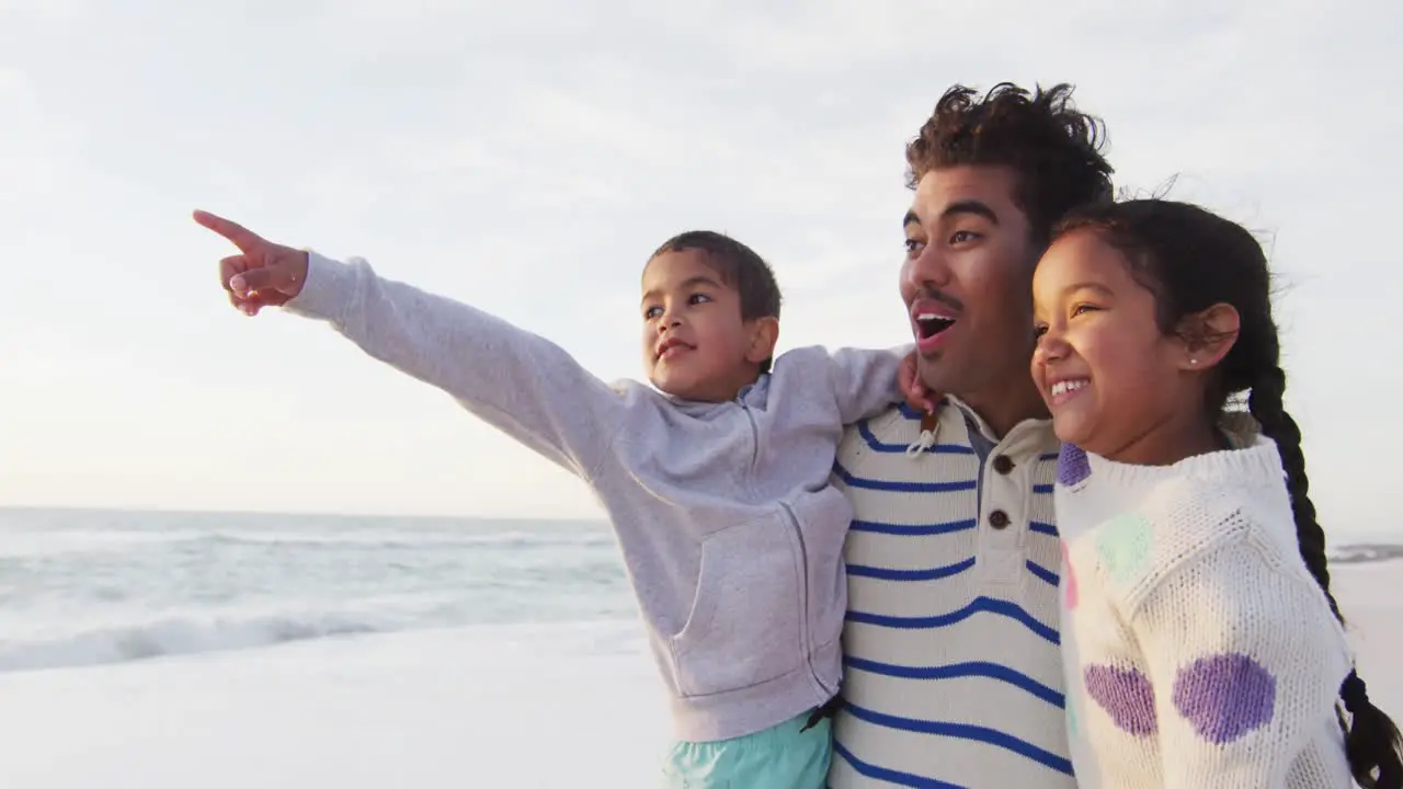 Happy hispanic father daughter and son looking at sunset on beach