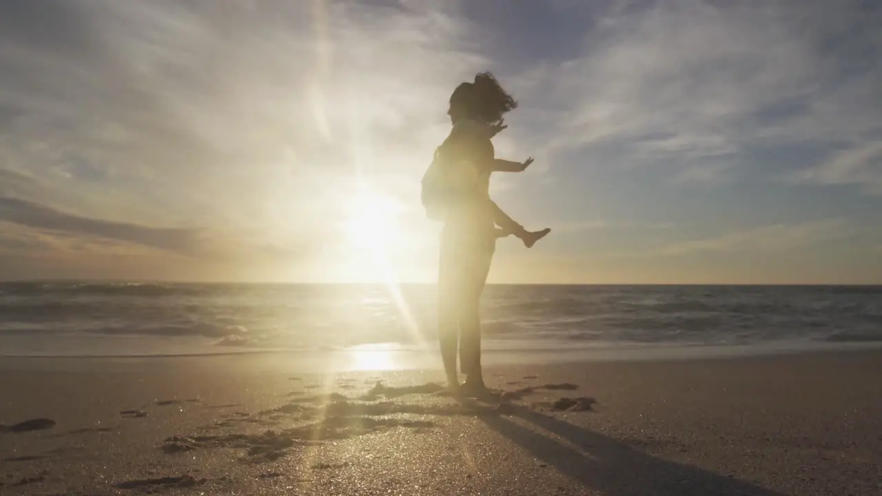 Happy hispanic mother having fun with daughter at sunset on beach