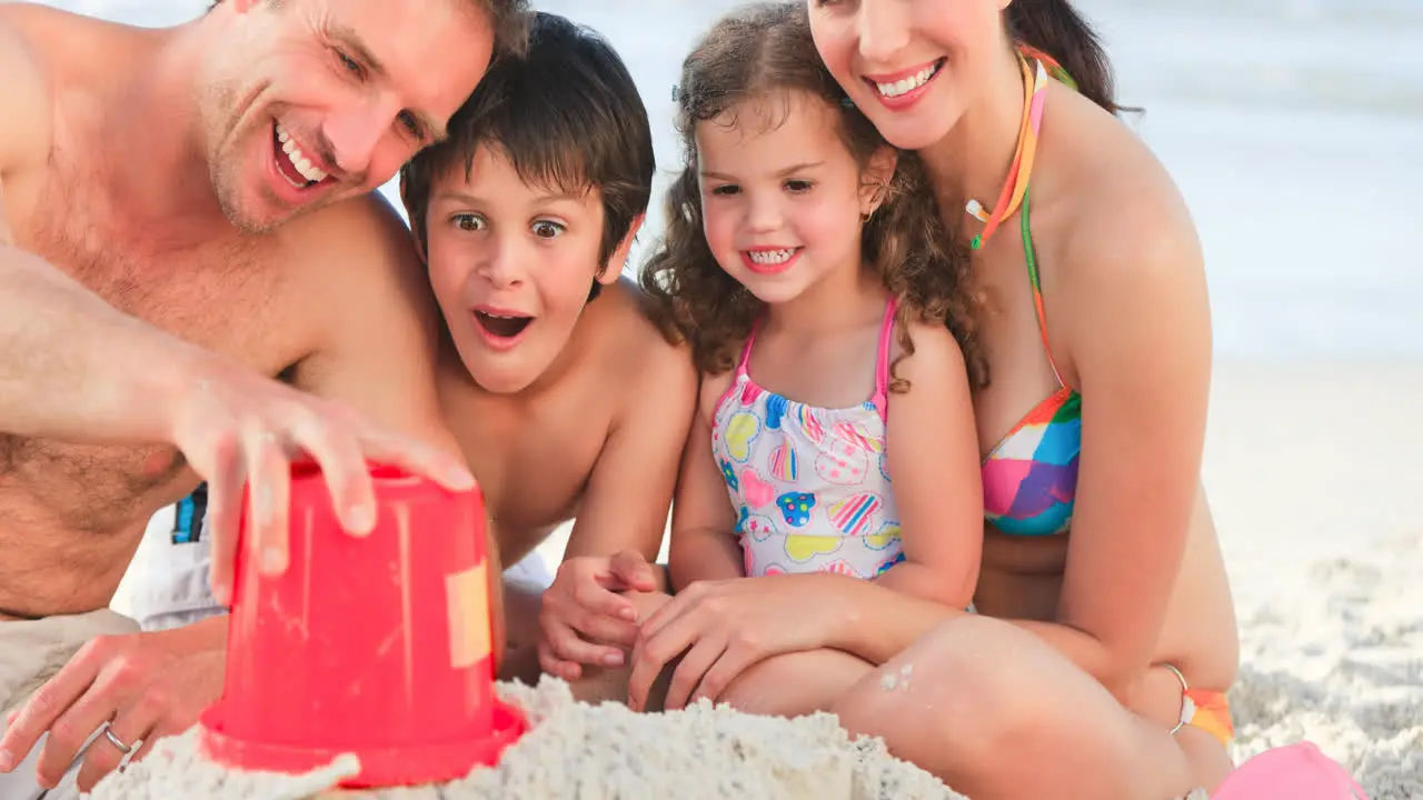 Portrait of smiling caucasian family on holiday playing with sand by sea