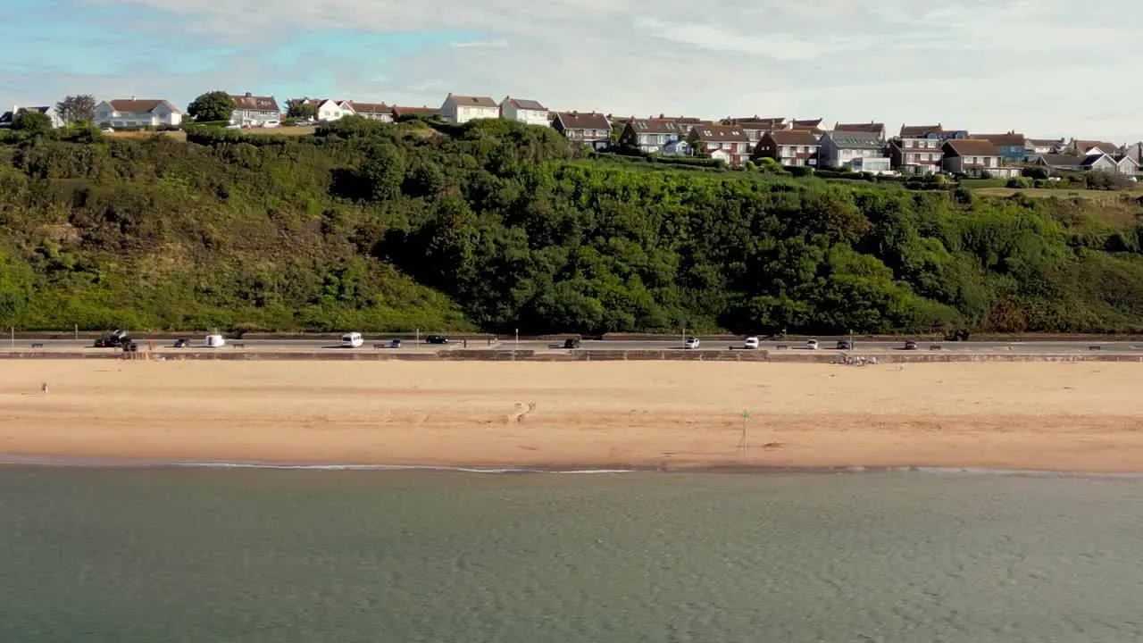 Panning drone shot of Exmouth Beach Devon from over the water showing Marine Drive Promenade and the Foxhole Hill residential area on top of the cliff