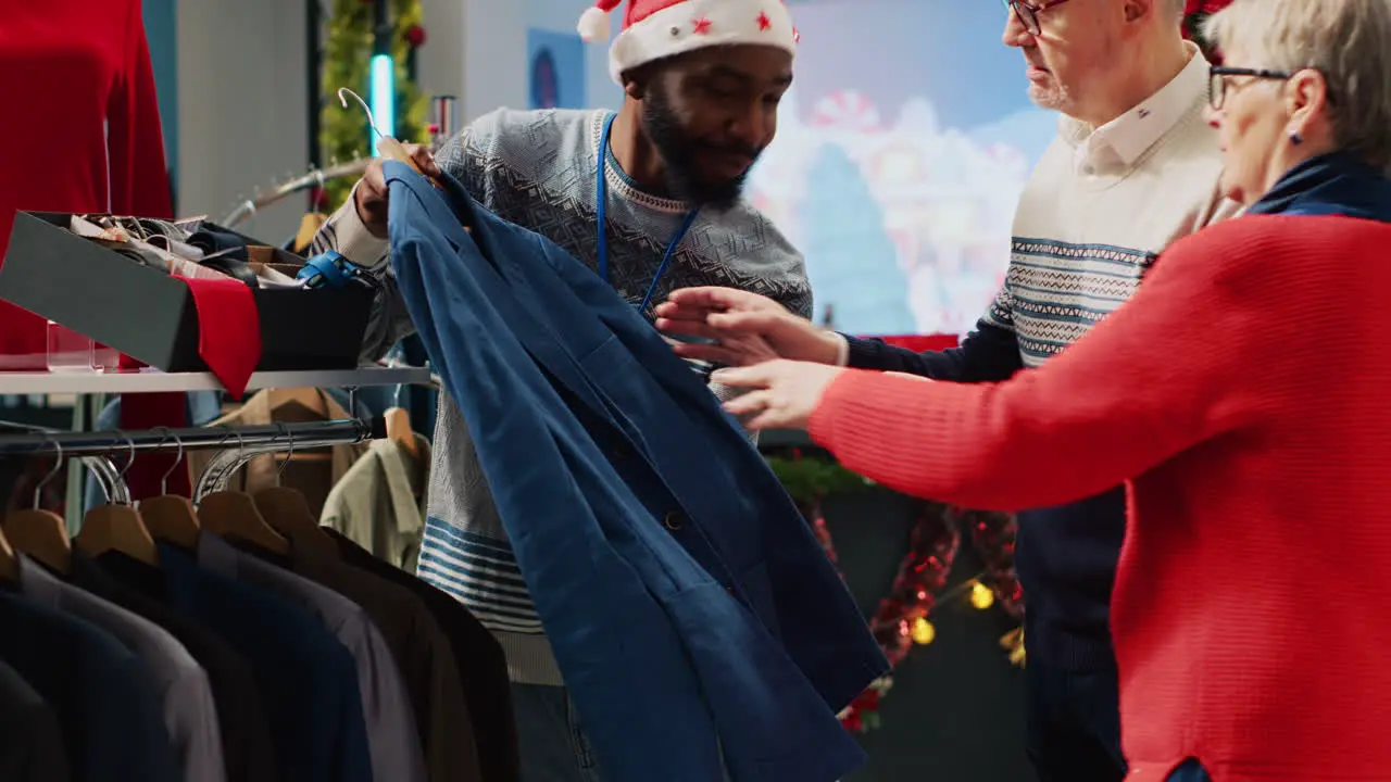 Retail assistant in xmas ornate clothing store helping senior couple during their Christmas frenzy shopping spree Worker offering advice to older clients during winter holiday season