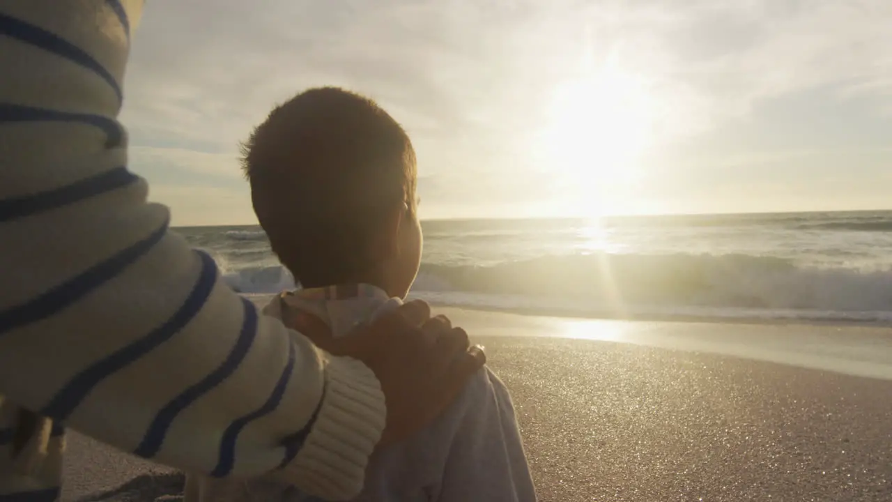 Back view of hispanic father and son looking at sunset on beach