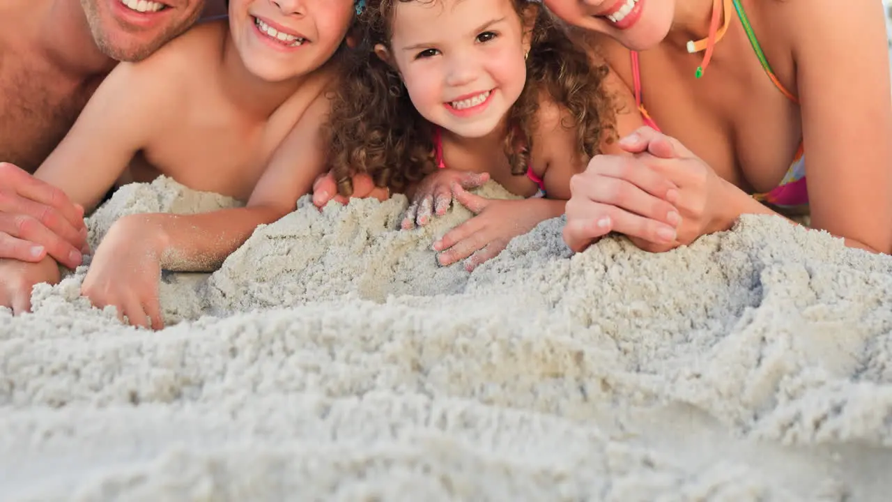 Portrait of smiling caucasian family on holiday lying on sand by sea