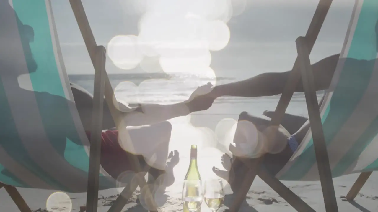 Animation of happy african american couple in sunbeds holding hands on beach